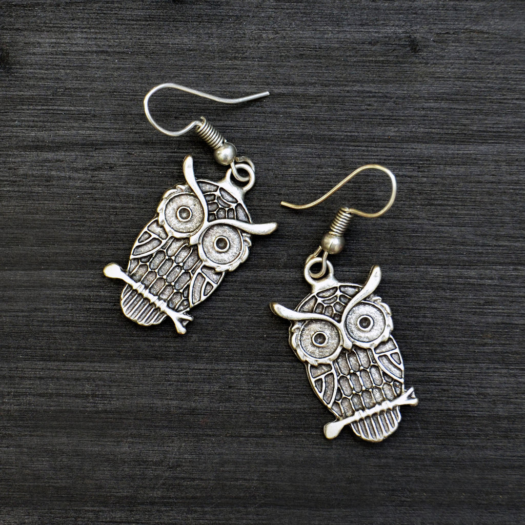 Small silver hanging owl earrings on black background