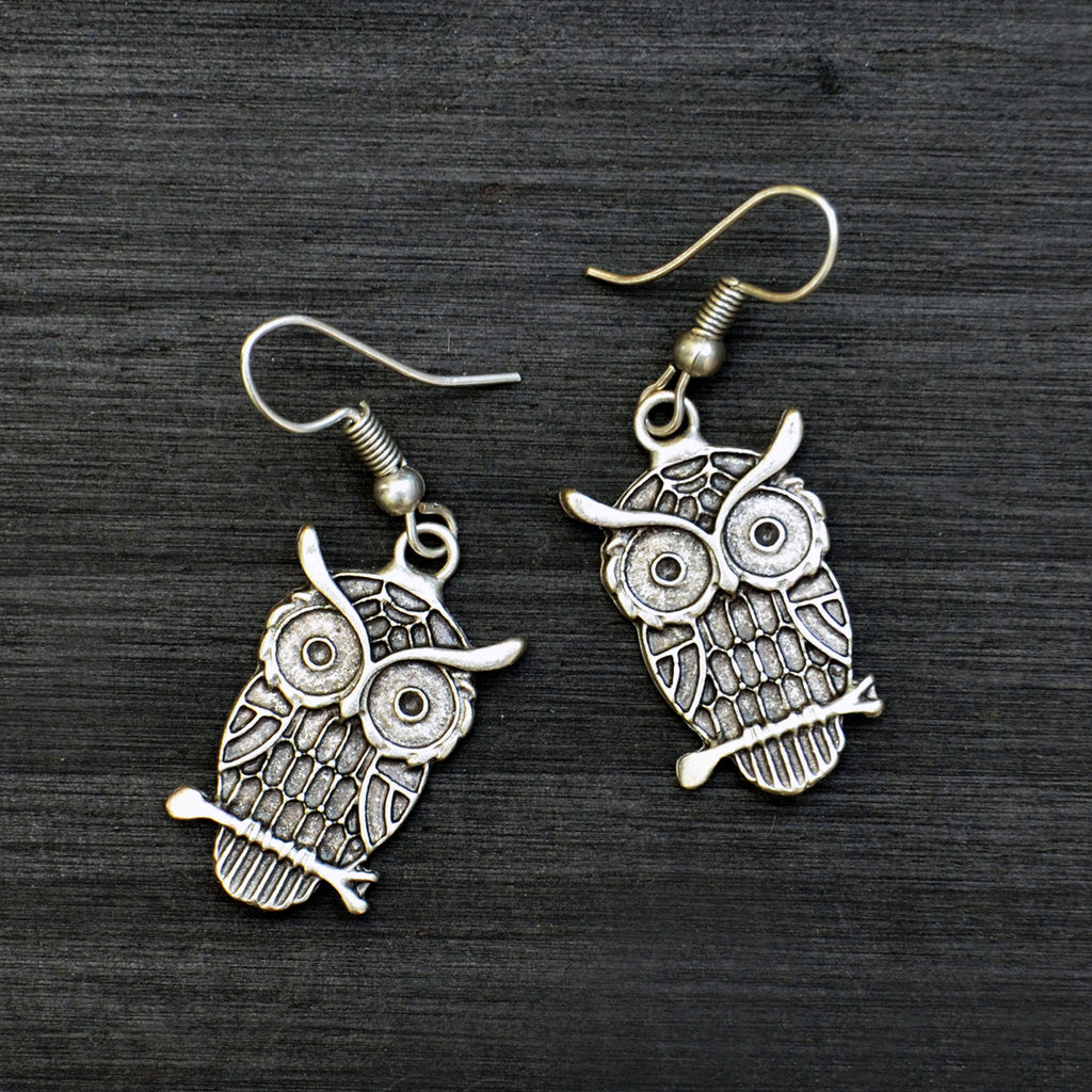 Small silver drop owl earrings on black background