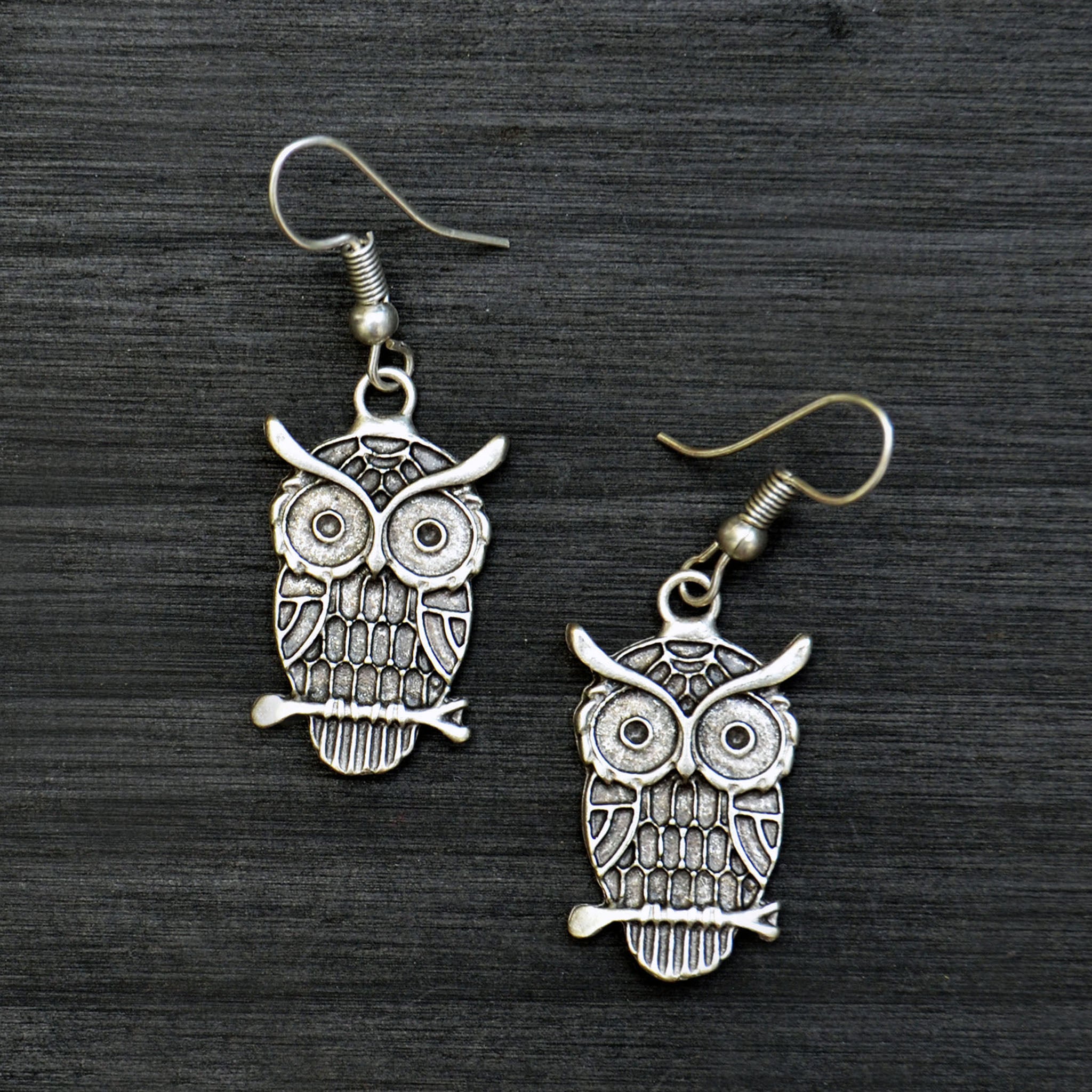 Small silver dangly owl earrings on black background