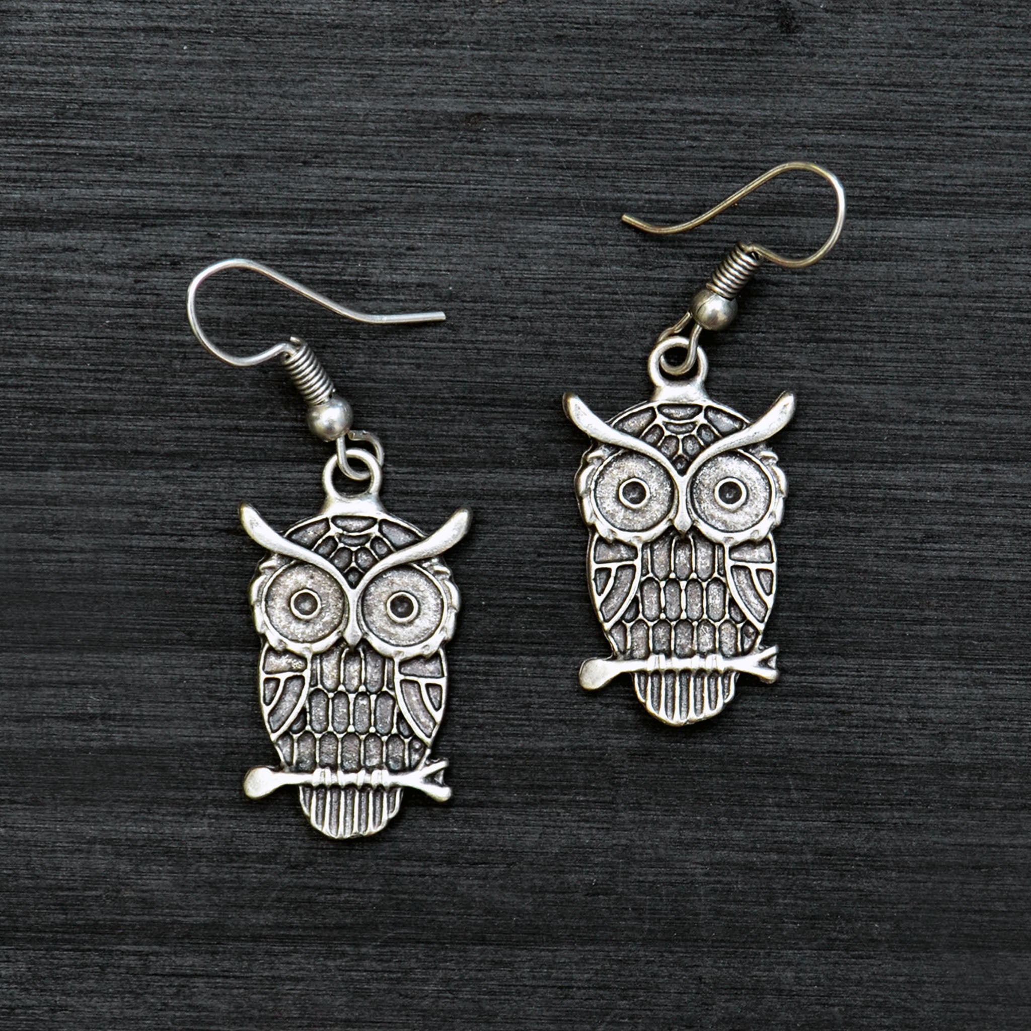 Silver dangle owl earrings on black background