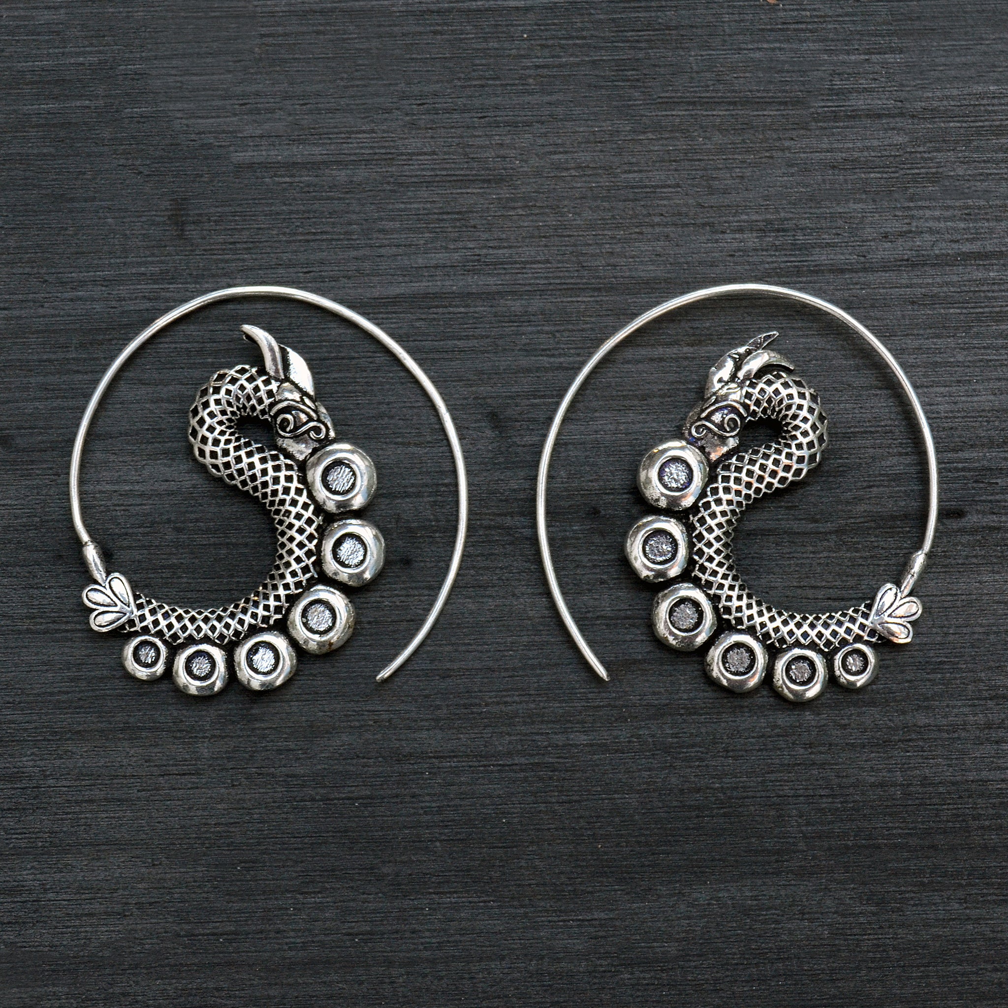 Spiral silver ethnic dagon earrings on black background