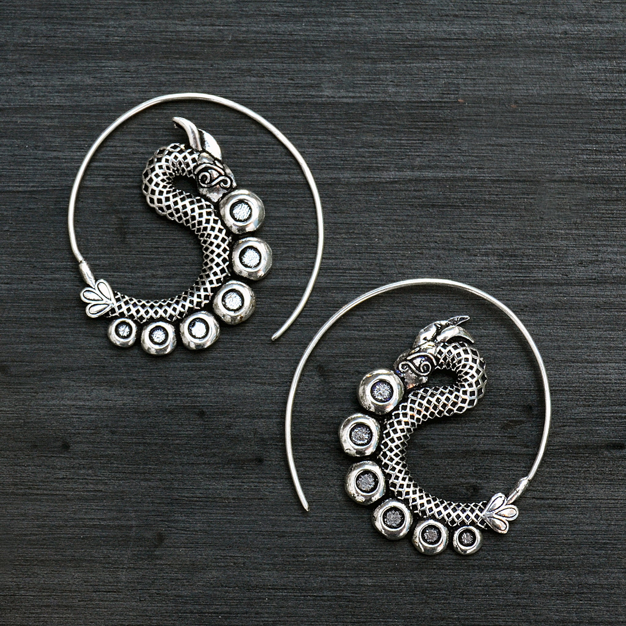 Tribal spiral silver dagon earrings on black background