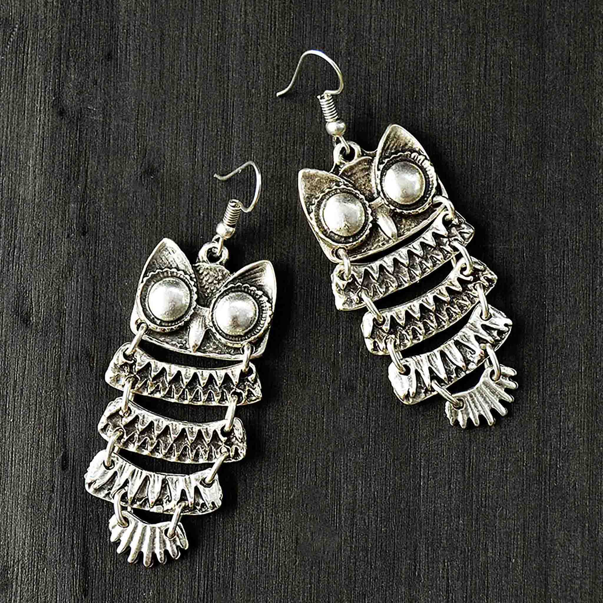 Silver hanging owl earrings on black background
