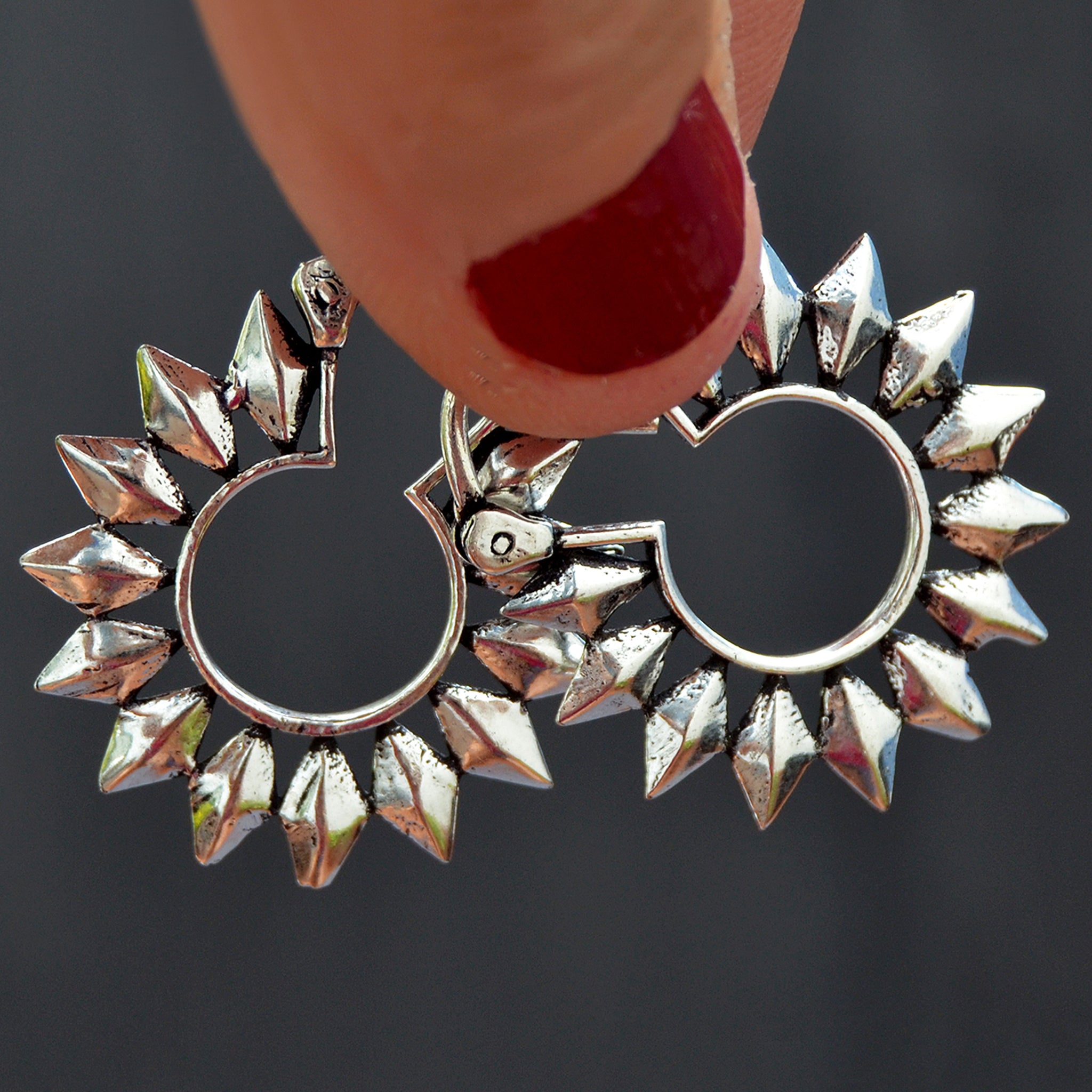 Small silver tribal sun hoop earrings on black background