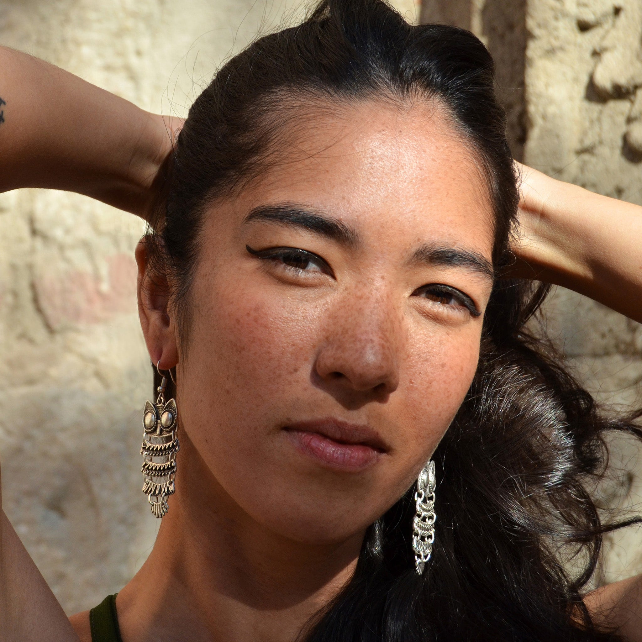 Young woman with long black hair wearing silver hanging owl earrings