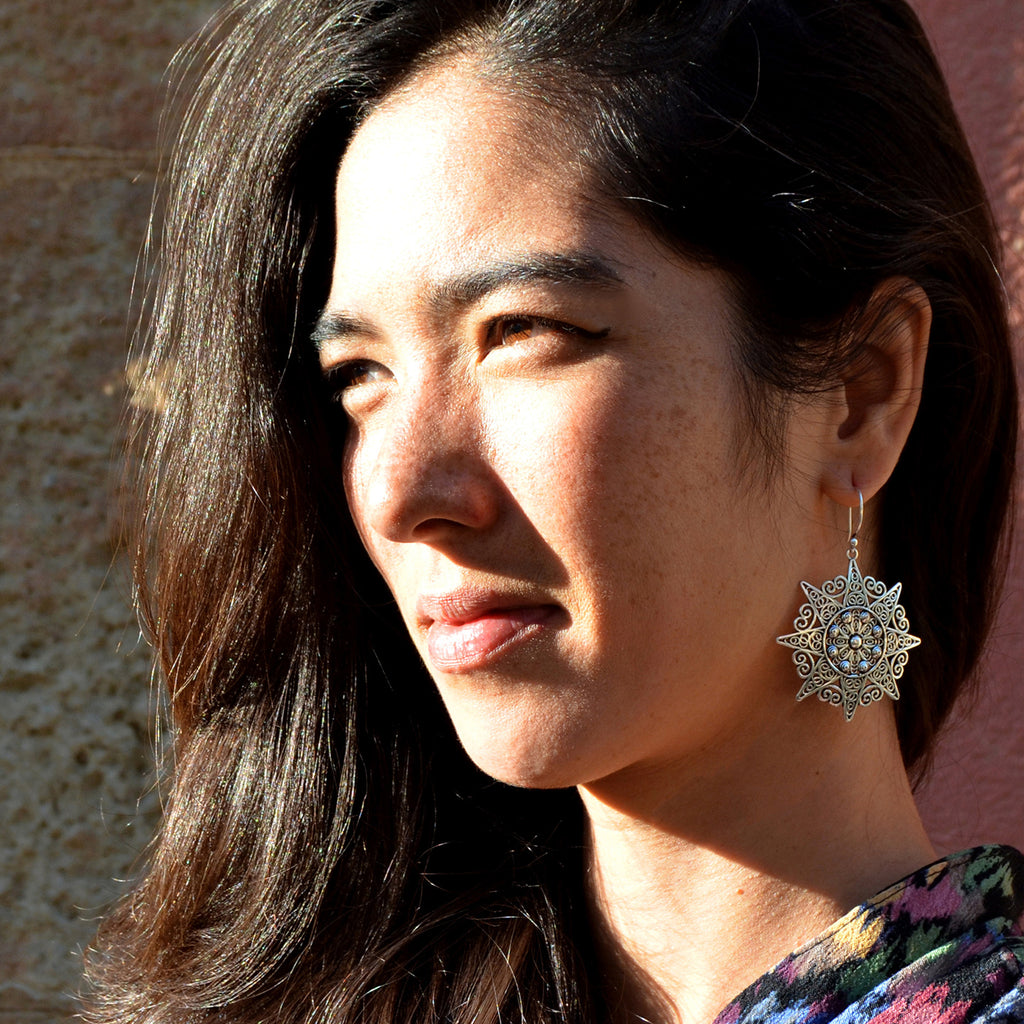 Young woman with black long hair wearing silver filigree mandala earrings