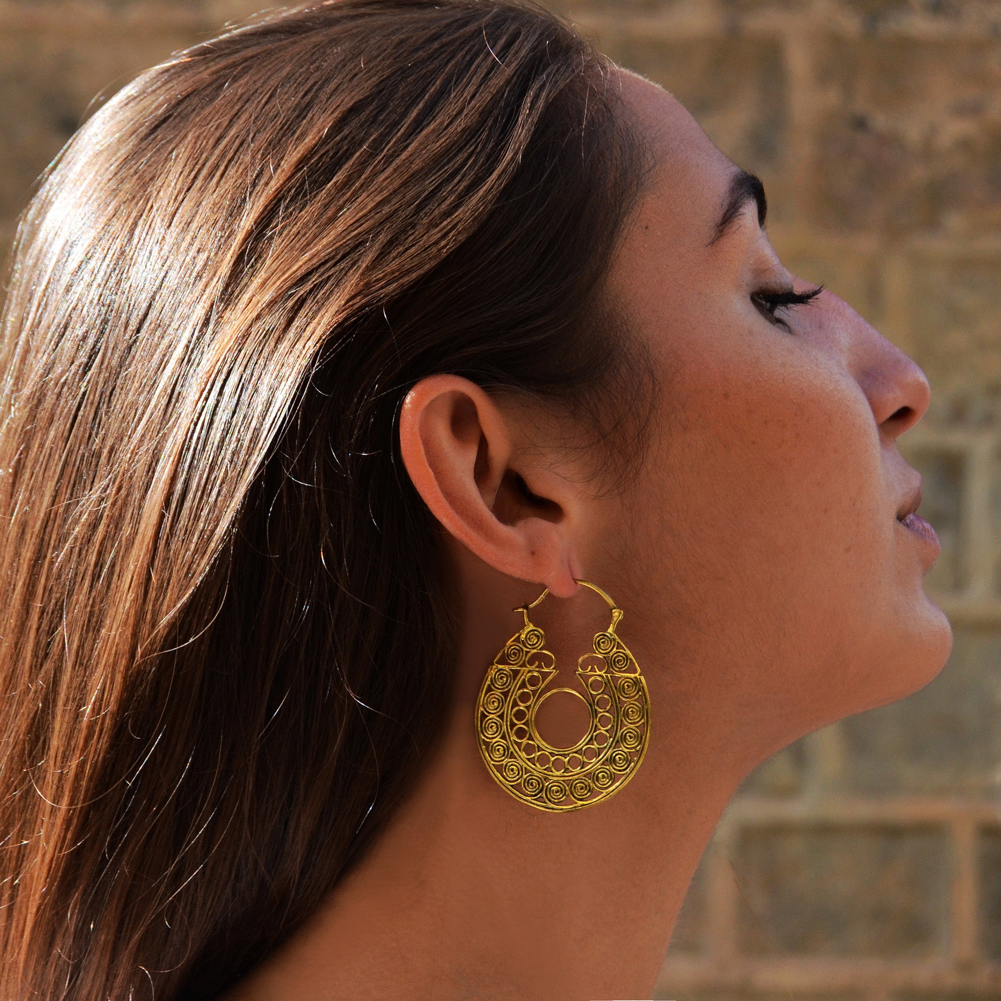 Young woman with long brown hair wearing brass filigree hoop earrings