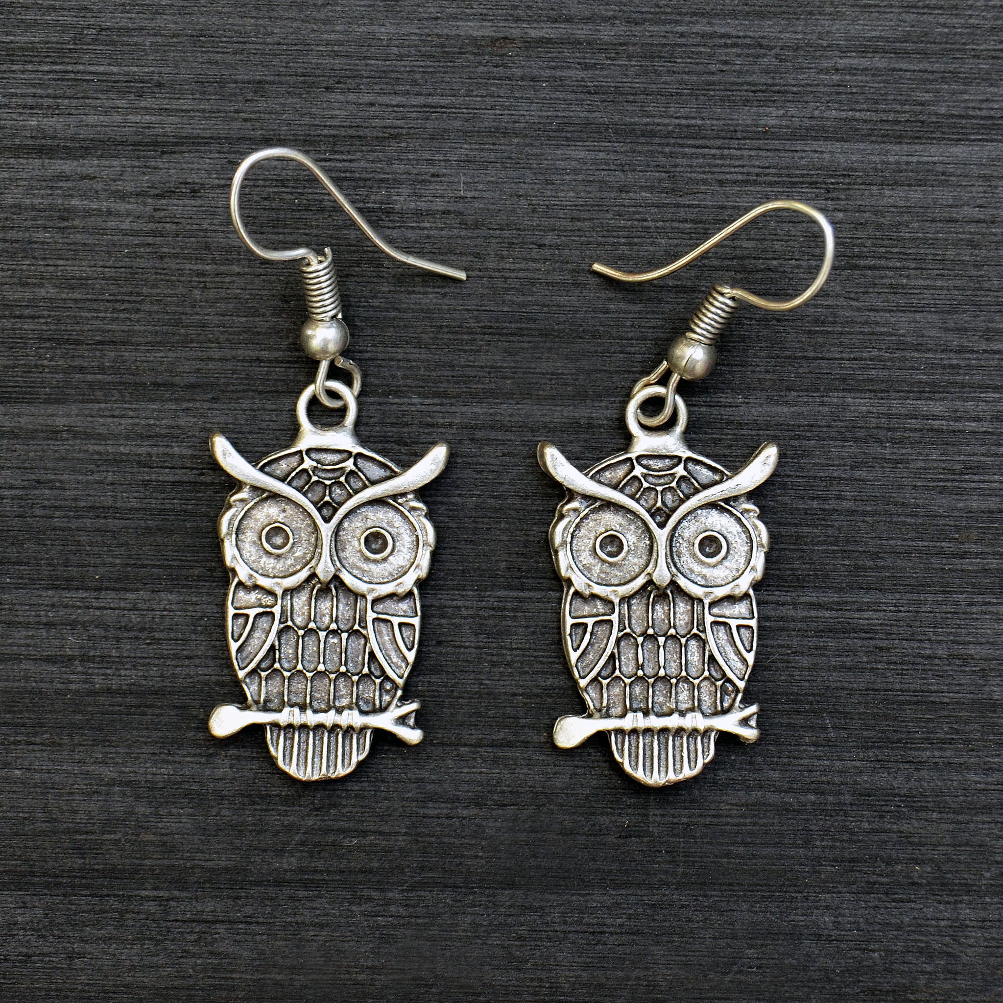 Small silver dangle owl earrings on black background