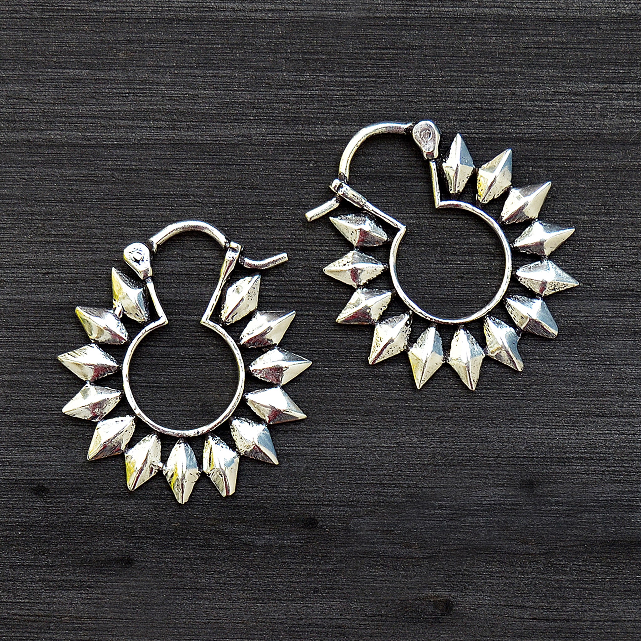 Small silver sun hoop earrings on black background
